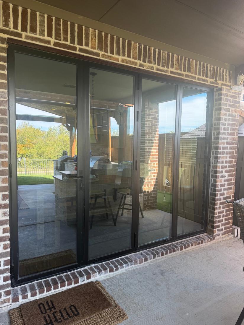 Custom black bifold glass patio door installed in a brick opening